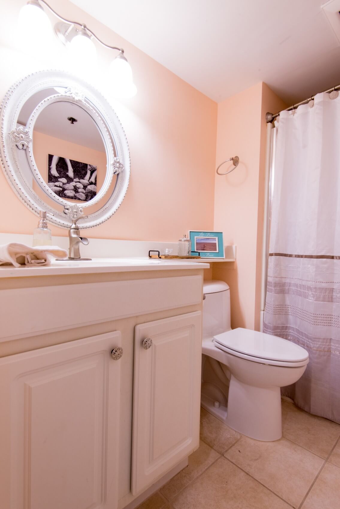 Sea Colony Condo Renovation Peach Color Bathroom with White Vanity Cabinet with White Top and Ornament Round Mirror
